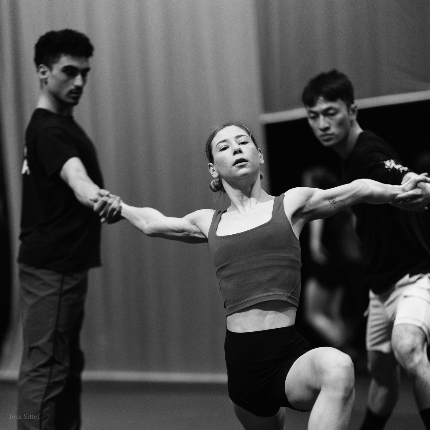 Melissa Panetta rehearsing in a studio with two other dancers, arms extended.