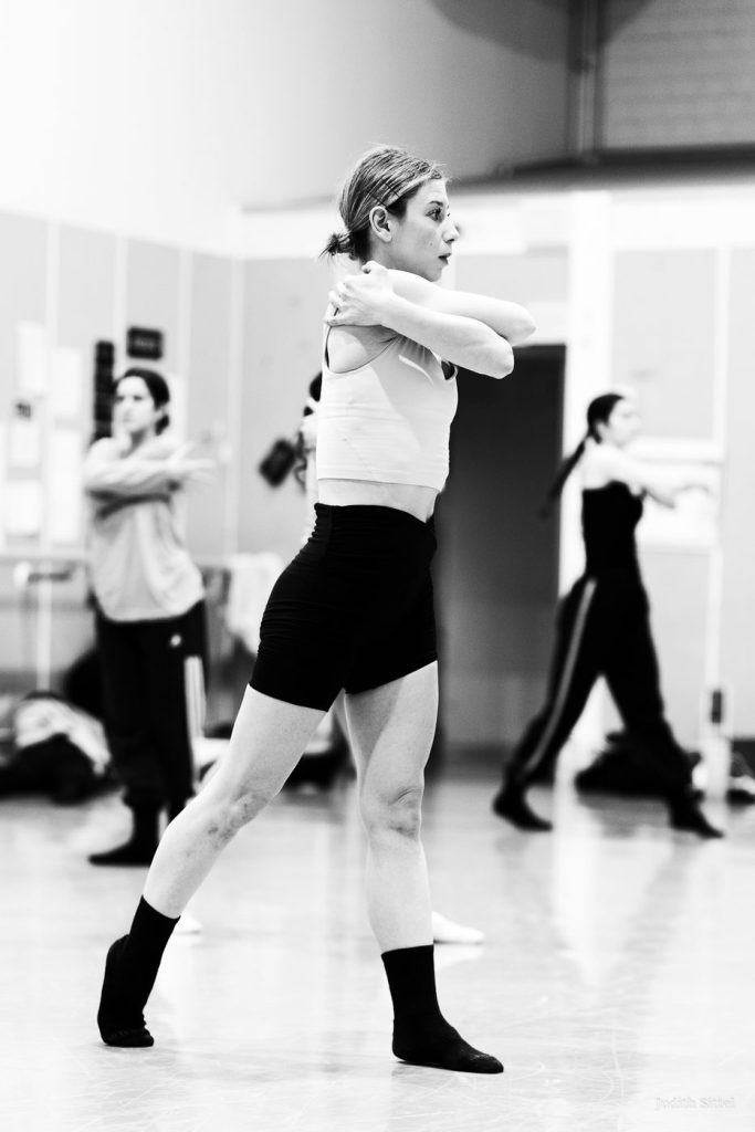 Melissa Panetta working in a company studio, dancers moving behind her.